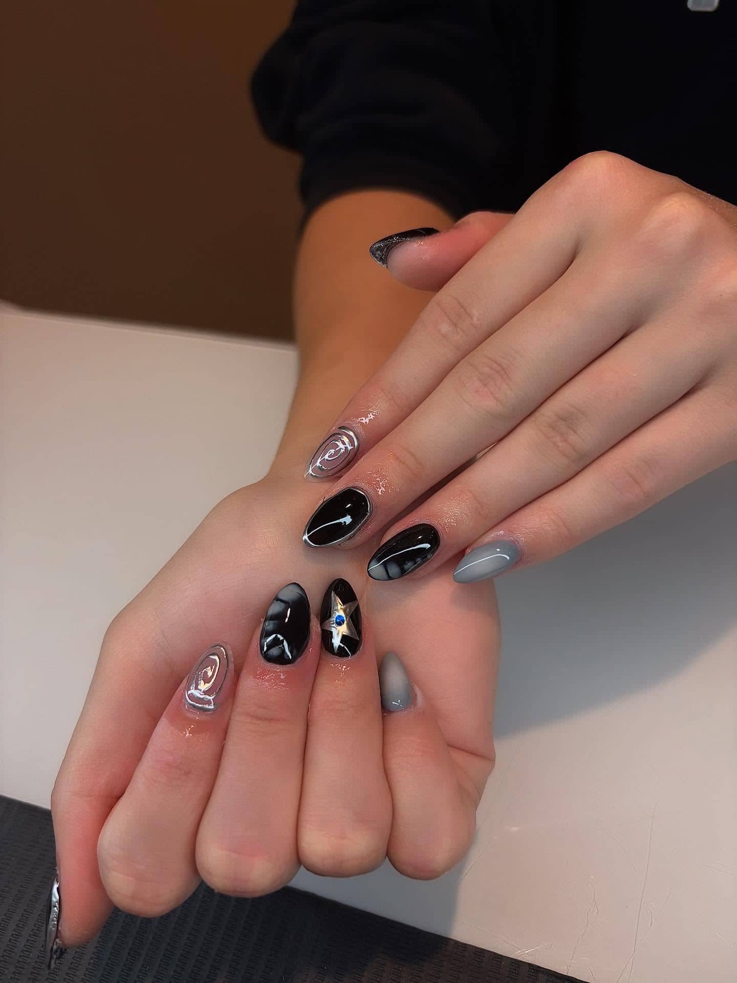 Short almond set in glossy black with silver chrome swirls and a jeweled star accent.