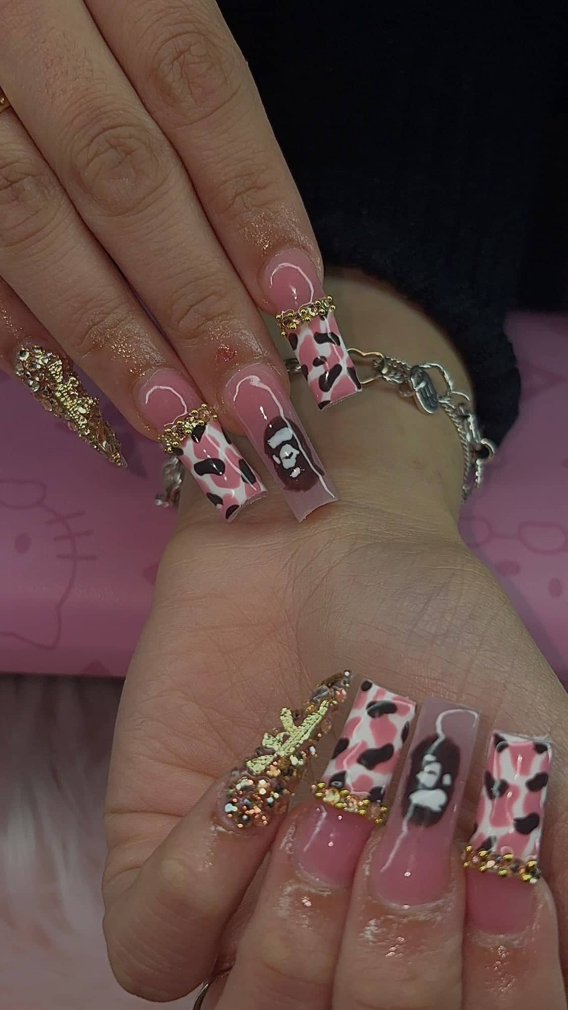 Long square set with pink-and-brown cow-print tips, gold bead and rhinestone cuticle lines, a hand-painted cartoon ape accent and a rhinestone-covered gold charm.
