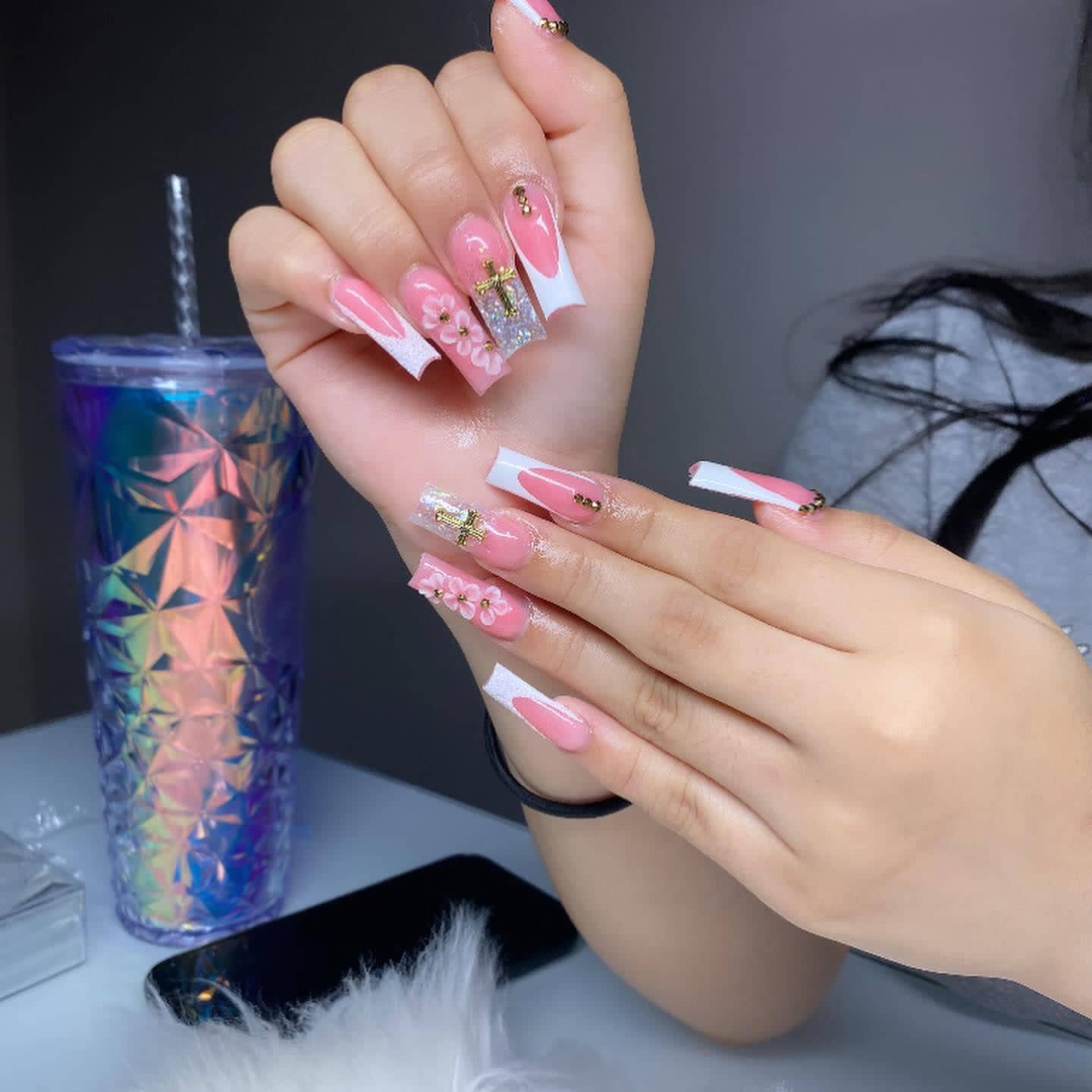 Long square pink set with white V-shaped French tips, a gold cross charm and pink 3D flowers.