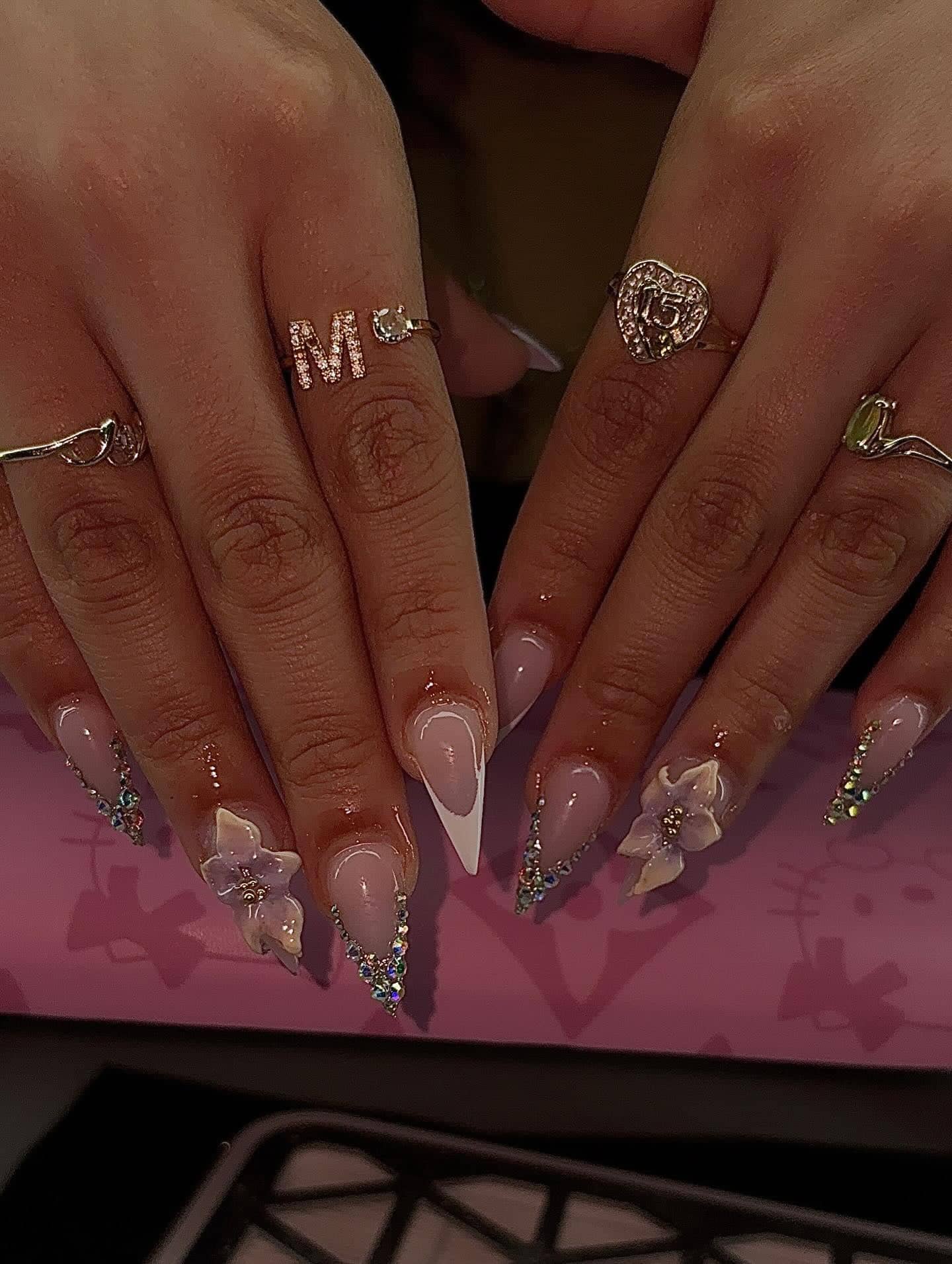 Stiletto set with white French tips, lavender 3D flowers and rhinestone-lined edges.