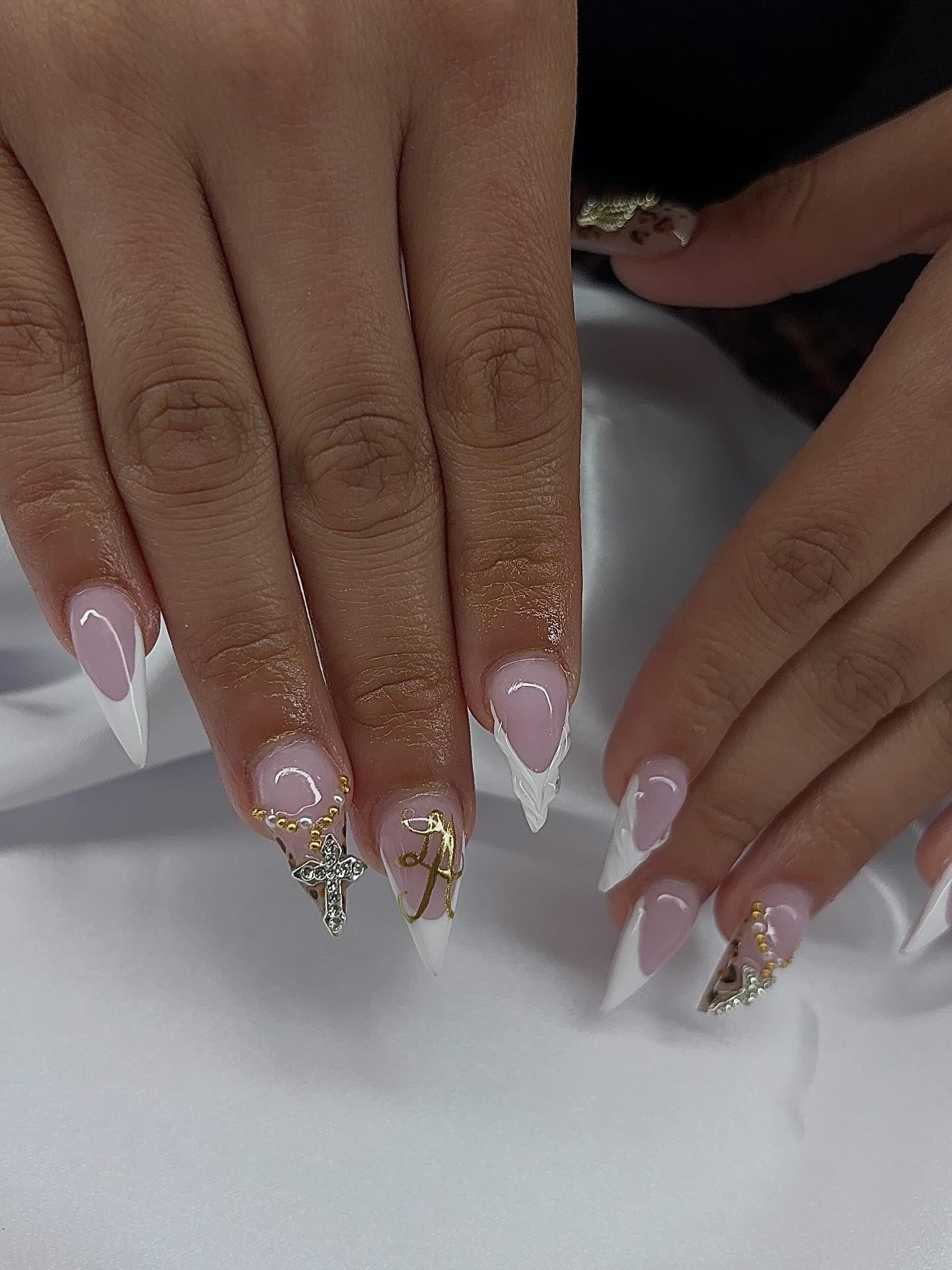 Stiletto set with white French tips, a gold initial charm, a cross charm and a pearl chain.