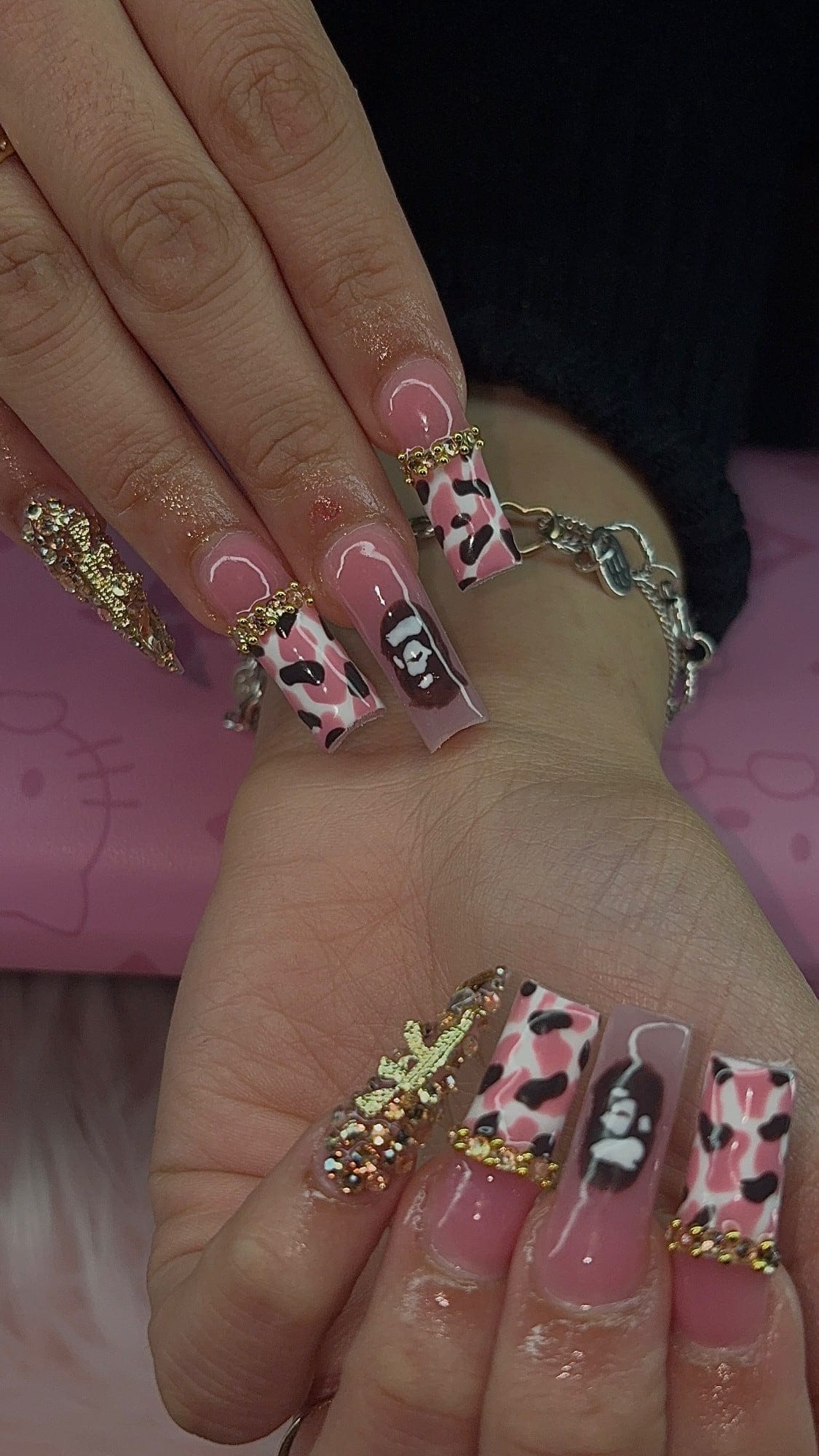 Long square set with pink-and-brown cow-print tips, gold bead and rhinestone cuticle lines, a hand-painted cartoon ape accent and a rhinestone-covered gold charm.