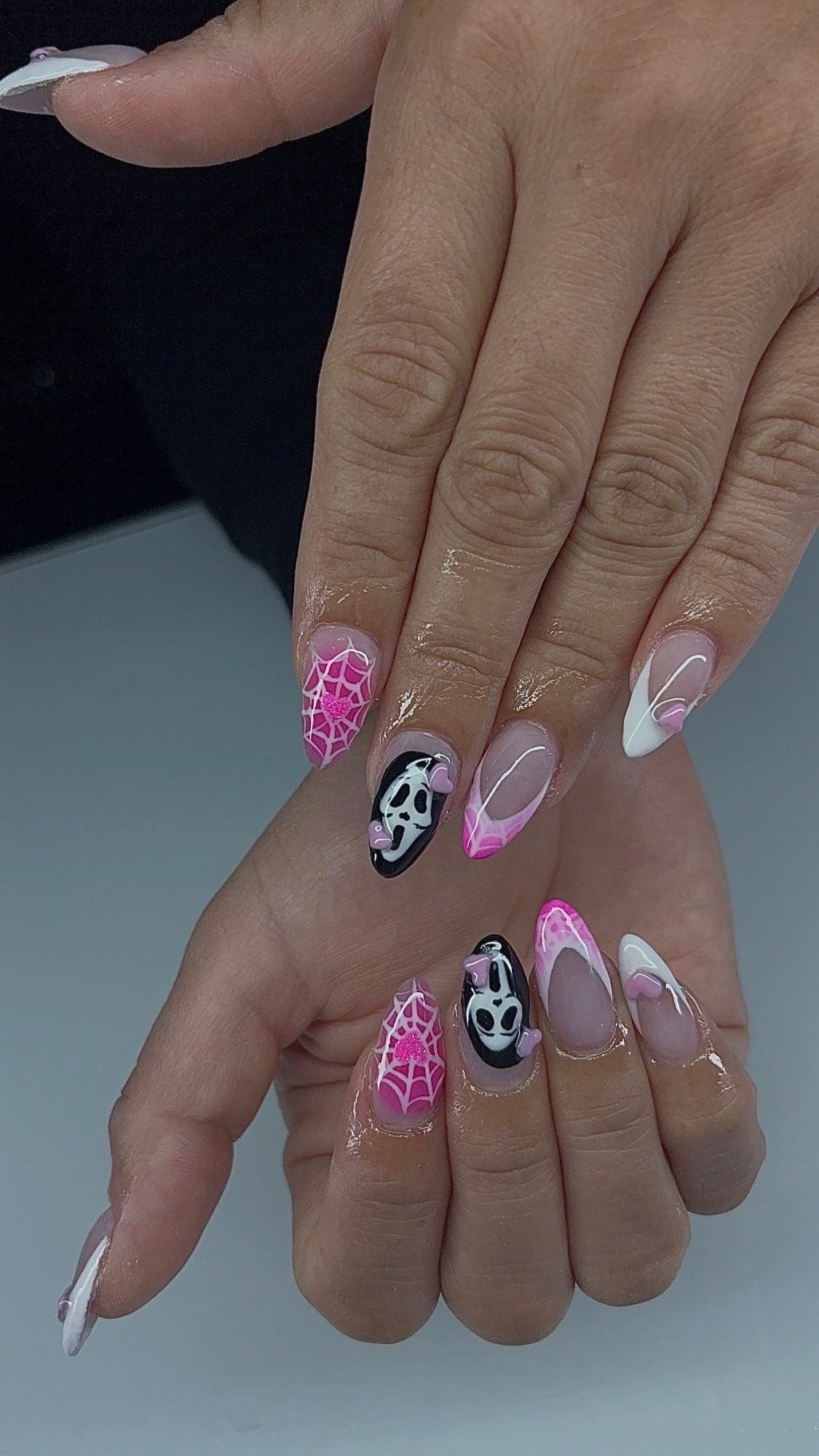 Almond Halloween set with pink spiderwebs, a pink glitter heart, hand-painted ghost-mask accents with lilac 3D hearts, and white French tips.
