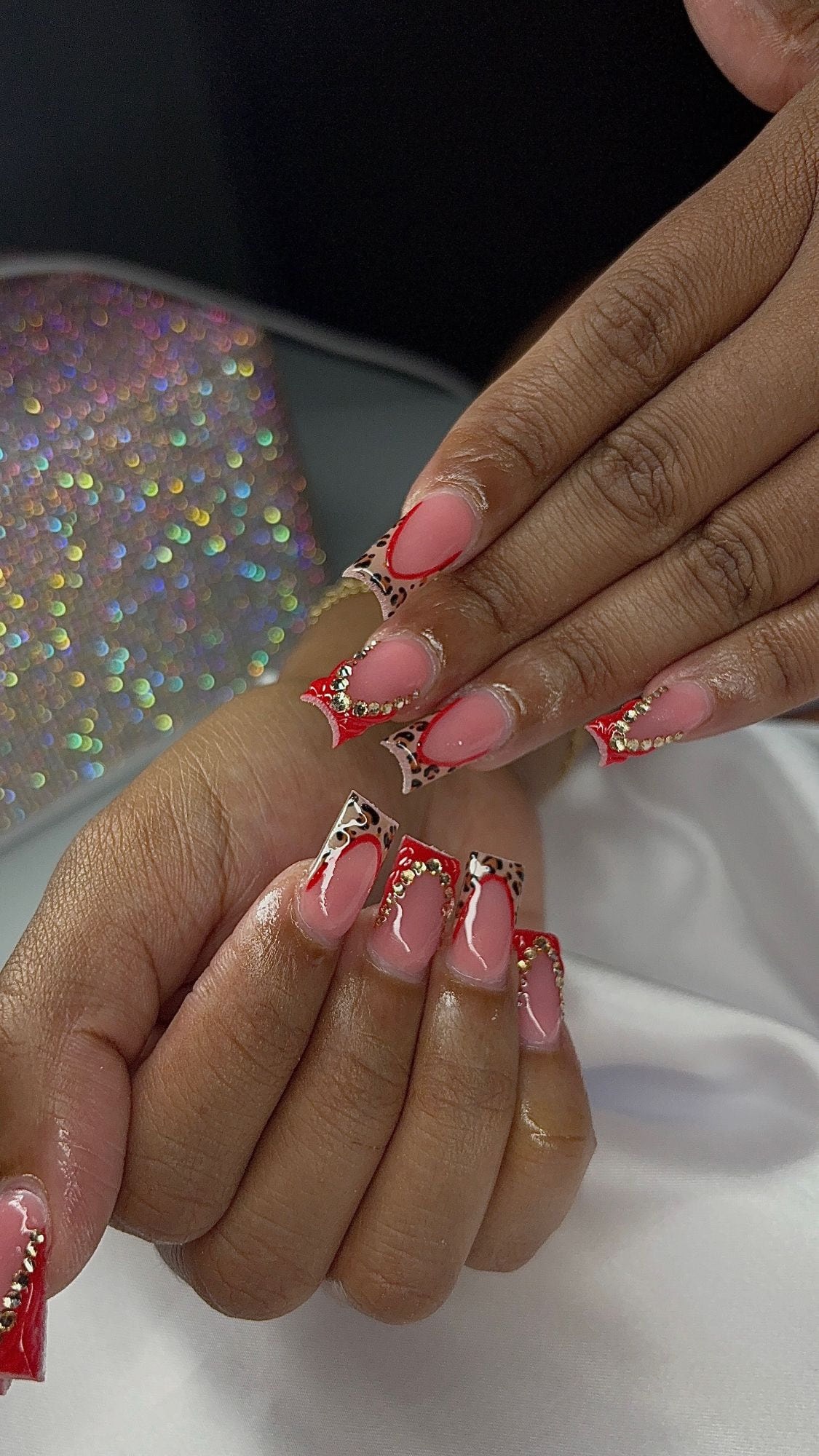 Square set with sheer pink bases, alternating red and leopard-print French tips outlined in red, and gold rhinestone accents.