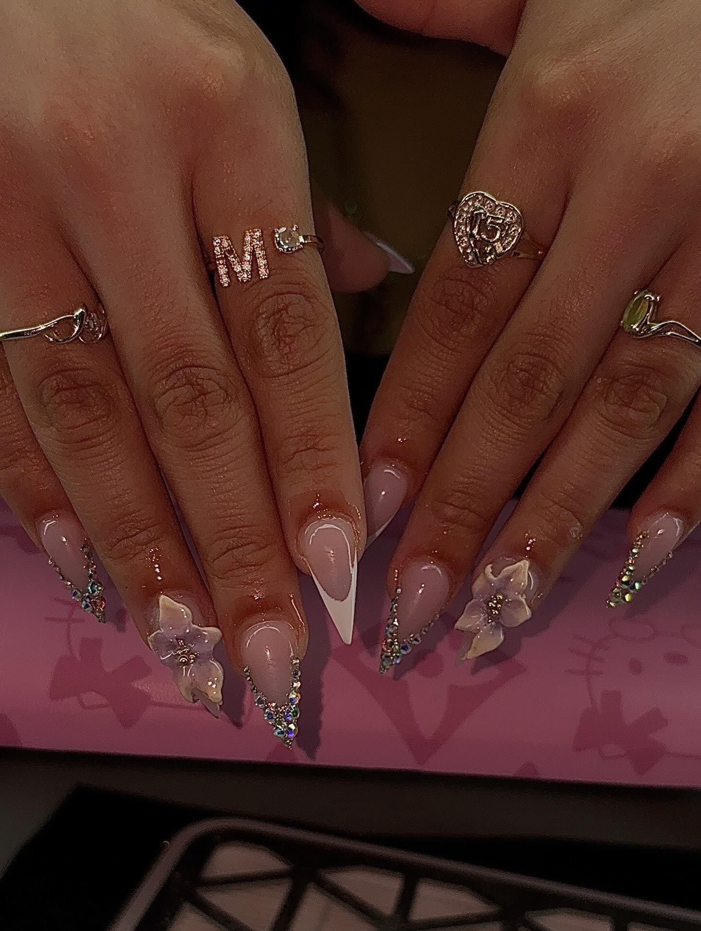 Stiletto set with white French tips, lavender 3D flowers and rhinestone-lined edges.