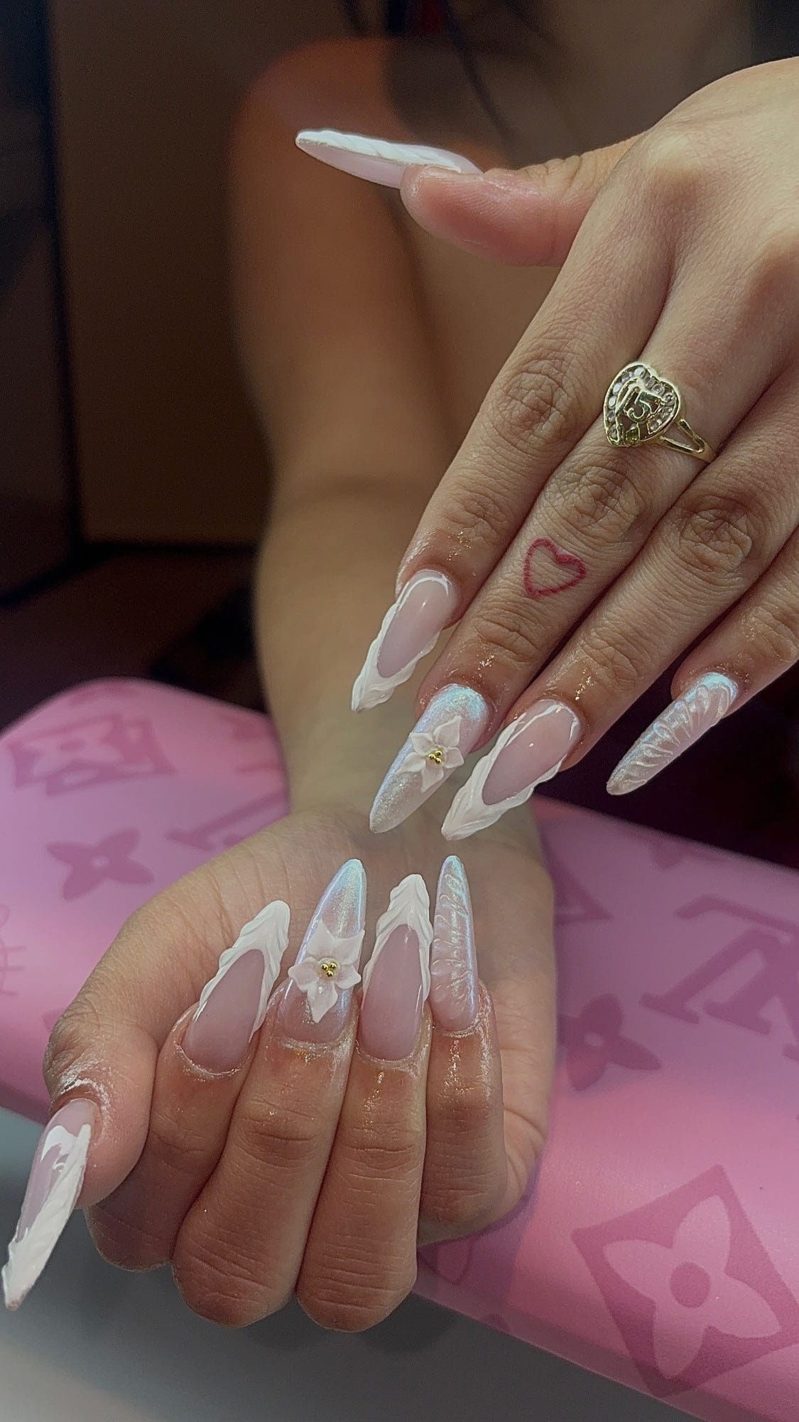 Long almond set with sheer pink bases, sculpted white 3D French tips, iridescent aurora glitter accents and a white 3D flower with gold beads.