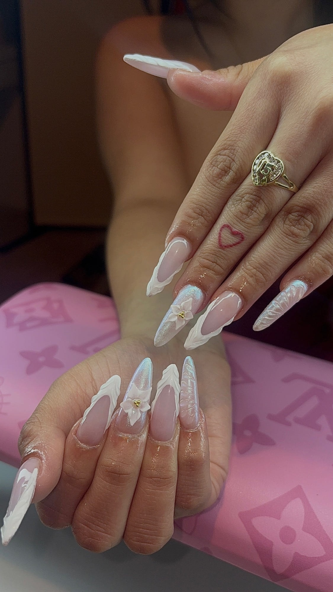 Long almond set with sheer pink bases, sculpted white 3D French tips, iridescent aurora glitter accents and a white 3D flower with gold beads.